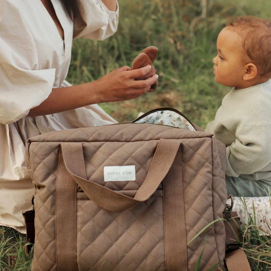 Mum and baby having a picnic on the grass with an Avery Row changing bag in Nutmeg